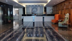 A modern reception area with a marble floor, a reception desk, and a seating area with an orange chair.