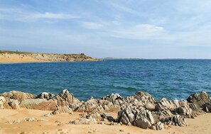Una playa rocosa con aguas azul cristalino y un promontorio lejano.