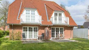 Ein zweistöckiges Haus mit rotem Ziegeldach, weißen Fensterrahmen und einer Ziegelaußenwand.