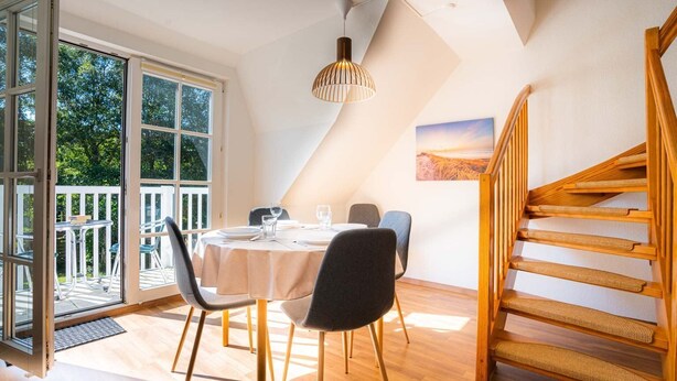 Ein Essbereich mit einem für vier Personen gedeckten Tisch, einer Holztreppe und Blick ins Freie durch große Fenster.