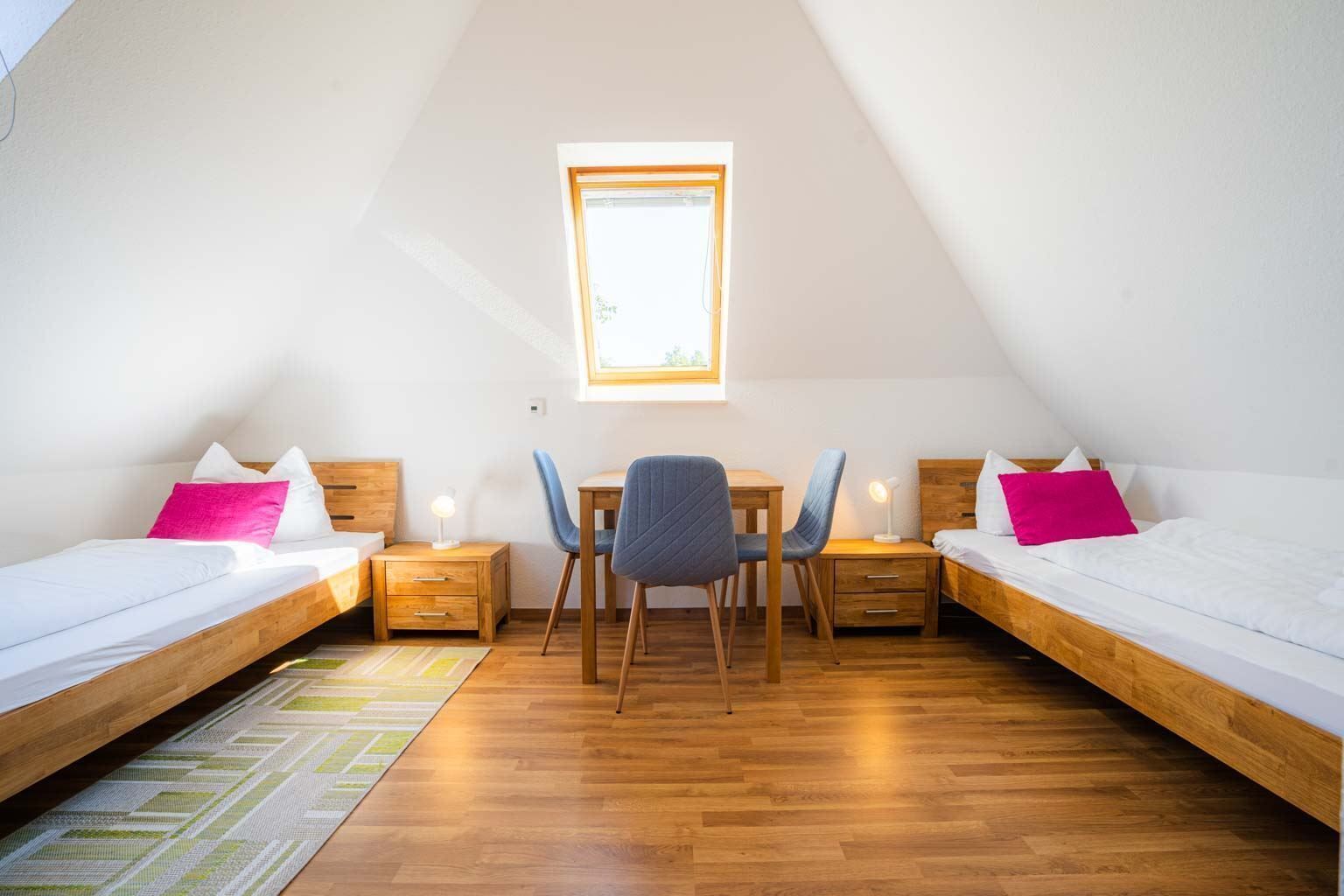 Een studentenkamer met twee eenpersoonsbedden, een bureau, twee stoelen, een klein tafeltje en een raam.