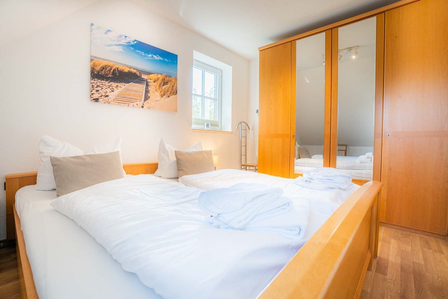 A bedroom with two beds, a wooden wardrobe, and a beach-themed painting on the wall.