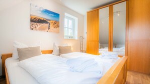 Ein Schlafzimmer mit zwei Betten, einem Holzschrank und einem Strandbild an der Wand.