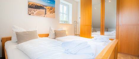 A bedroom with two beds, a wooden wardrobe, and a beach-themed painting on the wall.