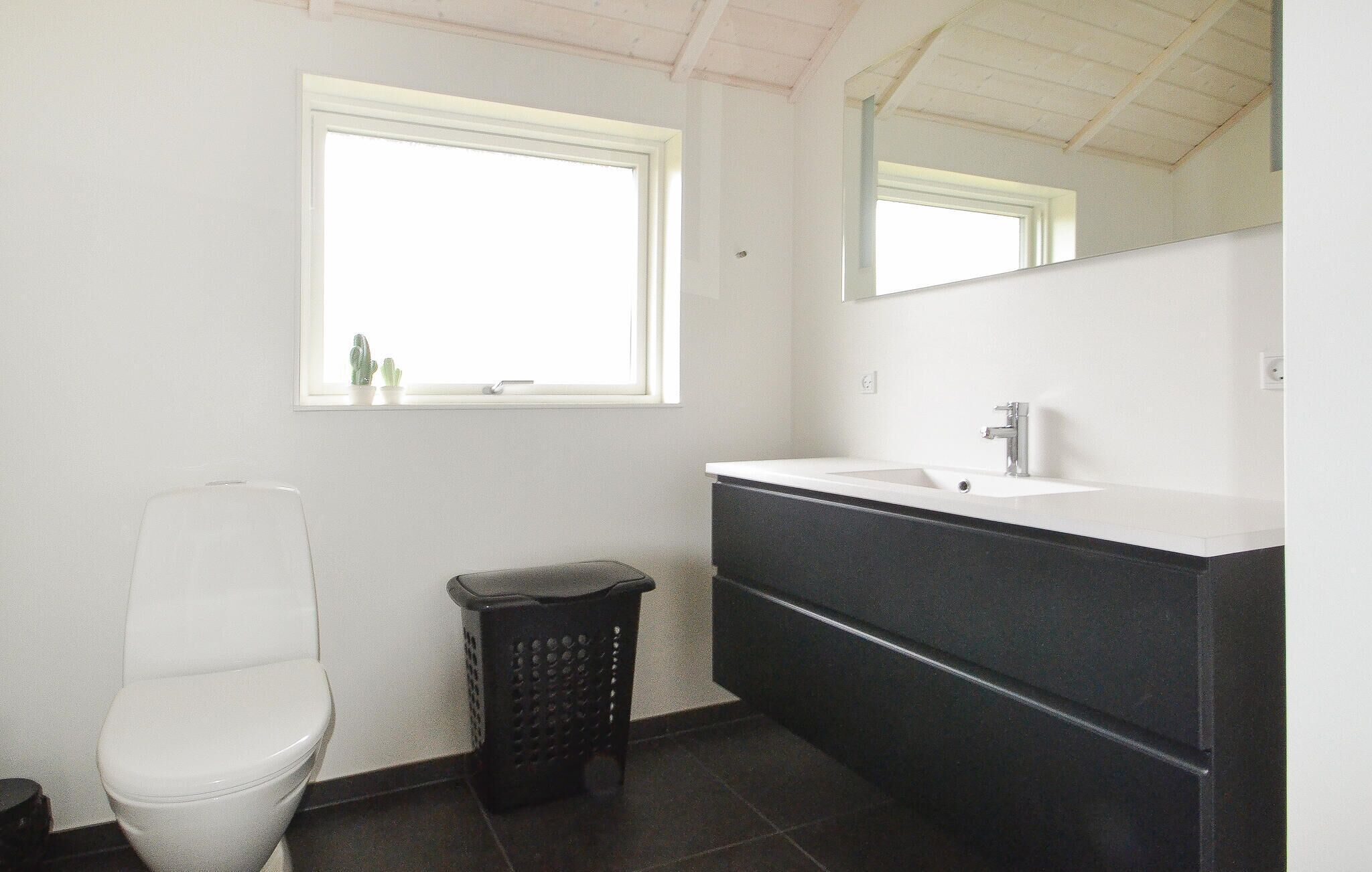 A bathroom with a toilet, a sink, a mirror, and a window.