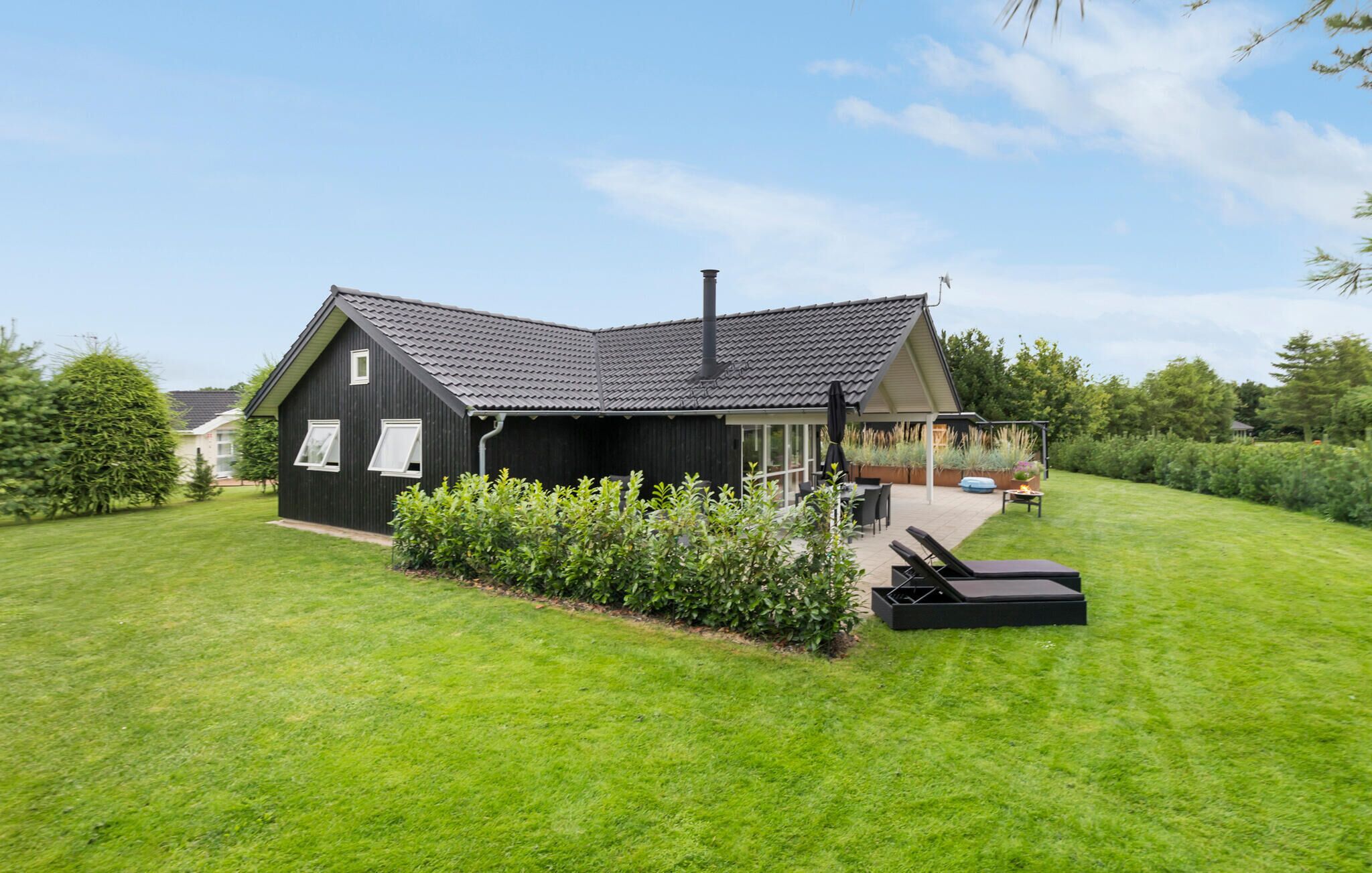 A modern house with a sloped roof, a patio with outdoor furniture, and a well-maintained lawn.
