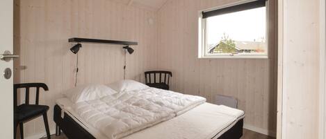 A bedroom with a bed, two chairs, a window, and a wooden ceiling.