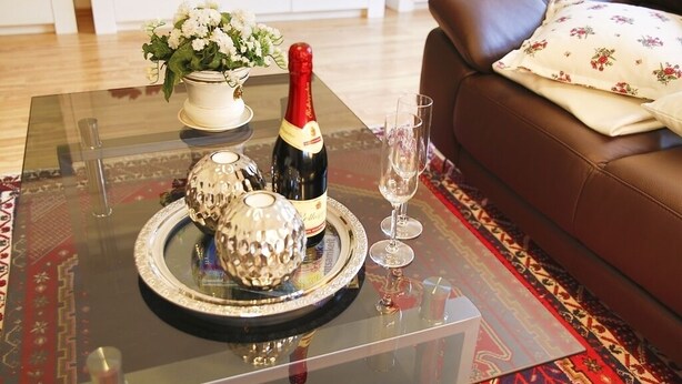 Una mesa de vidrio con una botella de champán, dos jarrones decorativos y una bandeja.