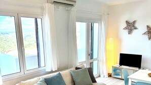 A modern living room with a sofa, chairs, a small table, and a TV. - Modern apartment with a fantastic view over the bay (Cala en Porter)