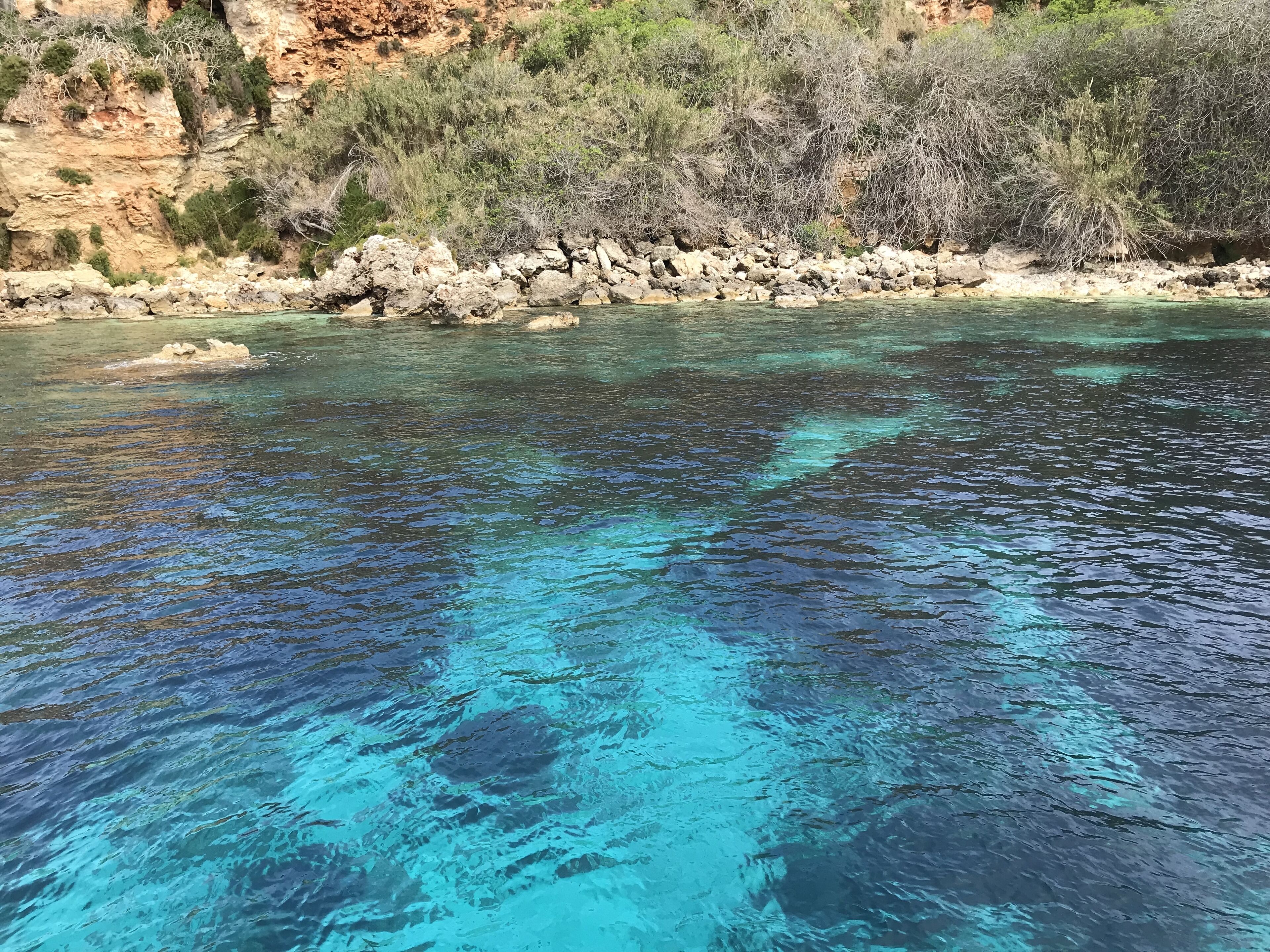 A clear, turquoise sea with rocky shores and sparse vegetation.