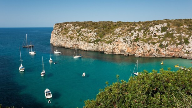 A coastal scene with boats anchored near a rocky cliff. - Modern apartment with a fantastic view over the bay (Cala en Porter)