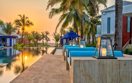 A poolside area with lounge chairs and a gazebo, surrounded by palm trees and modern buildings.
