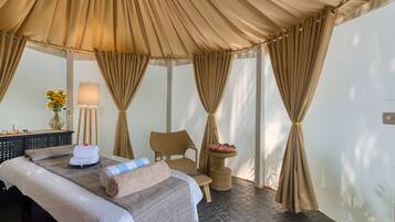 Relax in a serene space with a large bed, chair, and side table, featuring a canopy bed and a vase with flowers.