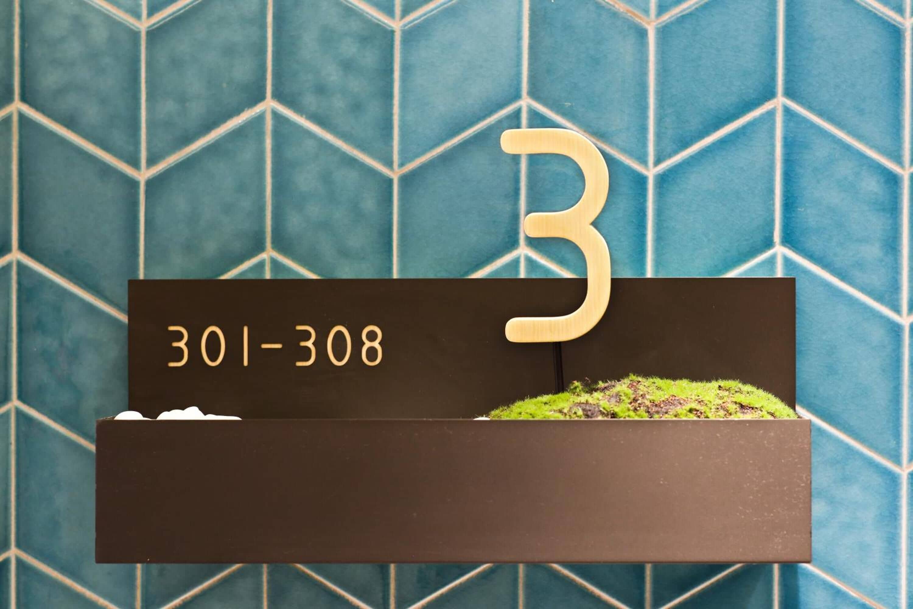 Naamplaatje van een hotelkamer met het nummer 3 en een kleine plantenbak met groene planten.