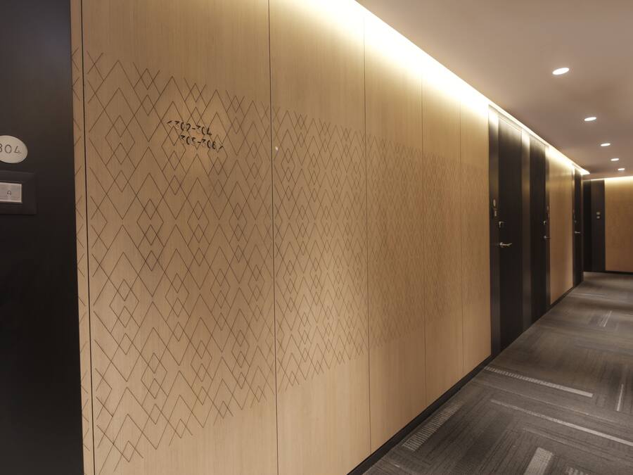 A hallway with patterned walls, a carpeted floor, and a door with a number sign.