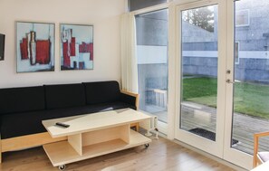 Un salon moderne avec un canapé noir, une table basse en bois clair et deux tableaux abstraits accrochés au mur.