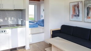 Eine kleine Küche mit Herd, Spüle und Fenster. Im Wohnbereich befindet sich ein dunkles Sofa und ein kleiner Tisch.