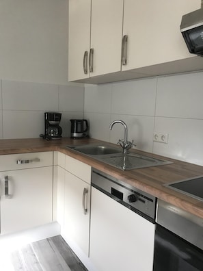 A modern kitchen with white cabinets, stainless steel appliances, and a wooden countertop.