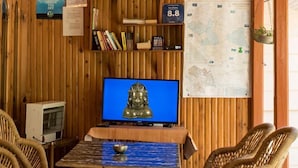 A room with a wooden wall, a television displaying a Buddha statue, a map, and a bookshelf. - Parvati Kuteer (Bhuntar)