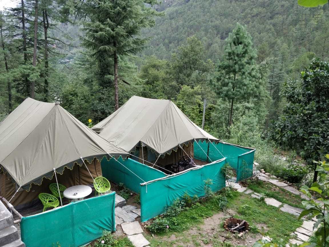 Two tents with attached seating, set in a forested area with a stone path.