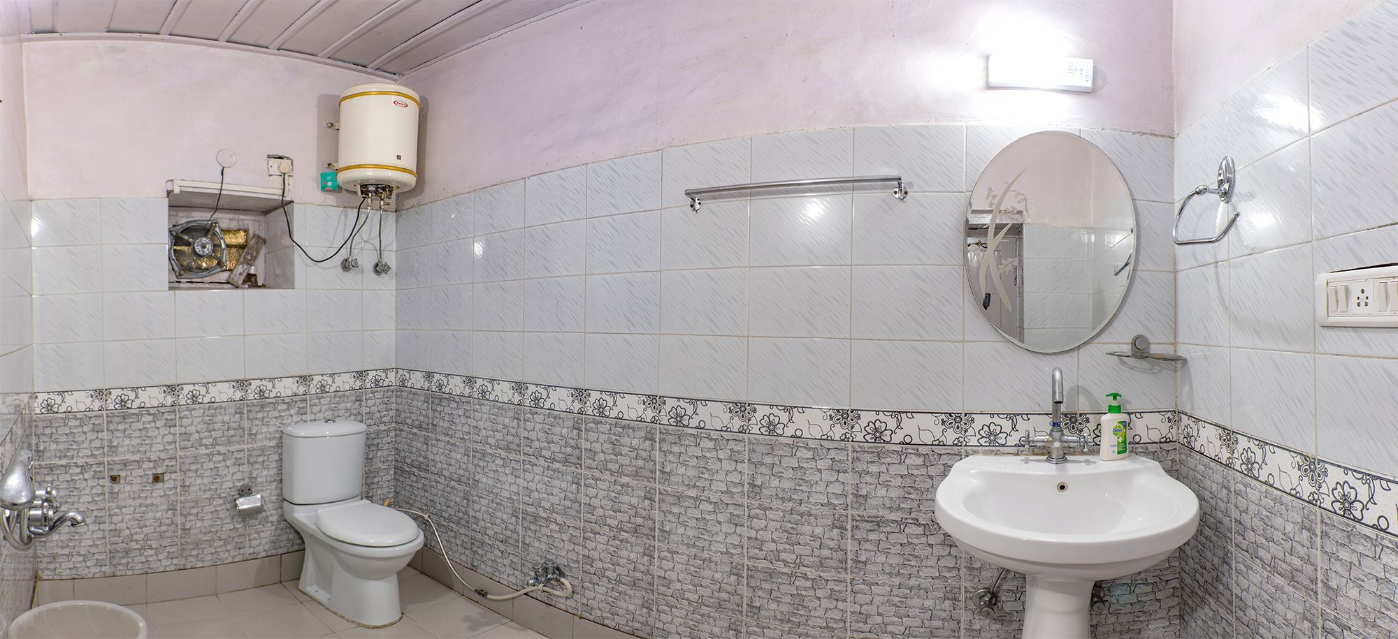 Et badeværelse med toilet, vask, spejl og bruser.