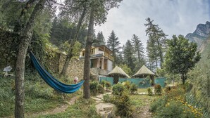 A rustic cabin with a balcony, surrounded by dense forest and a mountain backdrop. - Parvati Kuteer (Bhuntar)
