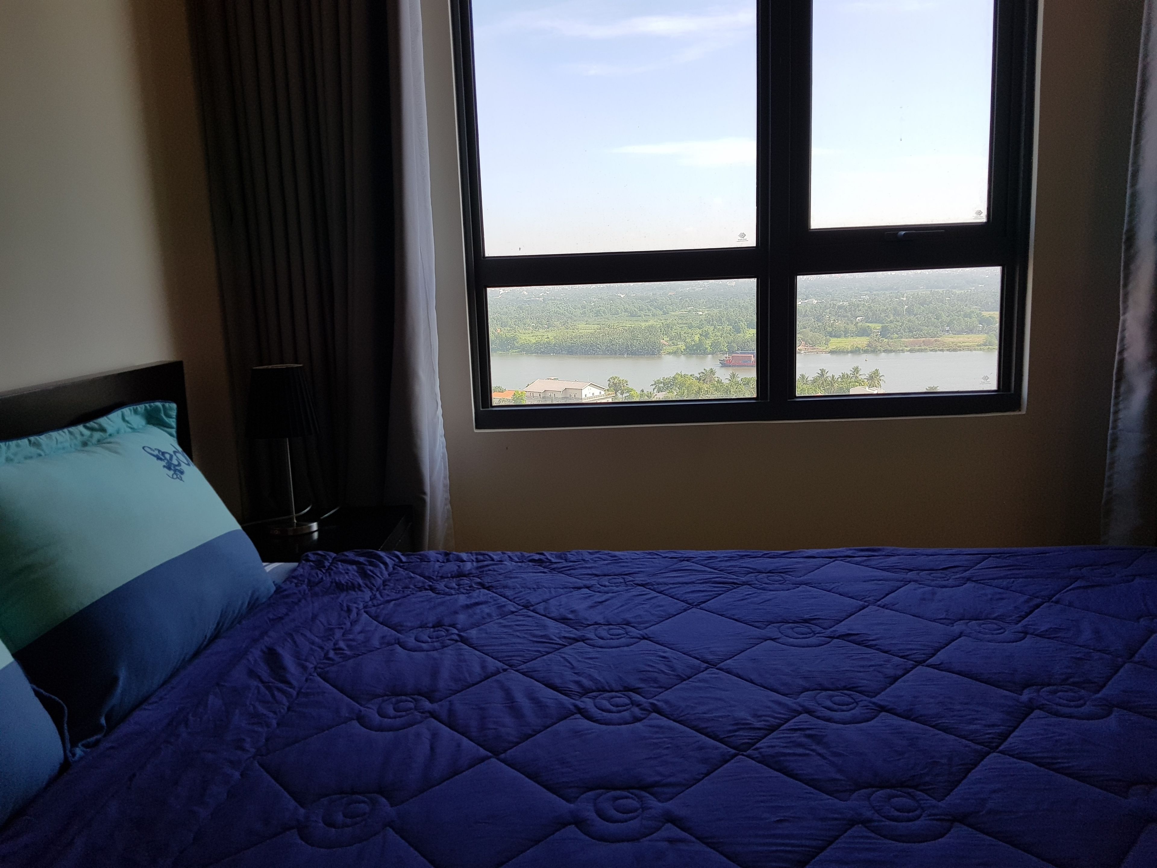 Ein Schlafzimmer mit Bett, Fenster und Blick auf einen See und Grünflächen.
