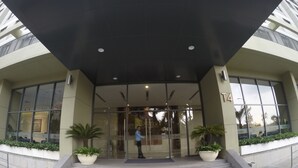 A modern building entrance with glass doors, a person standing at the entrance, and potted plants on either side. - Riverfront Osis Resort Balcony (Ho Chi Minh City)