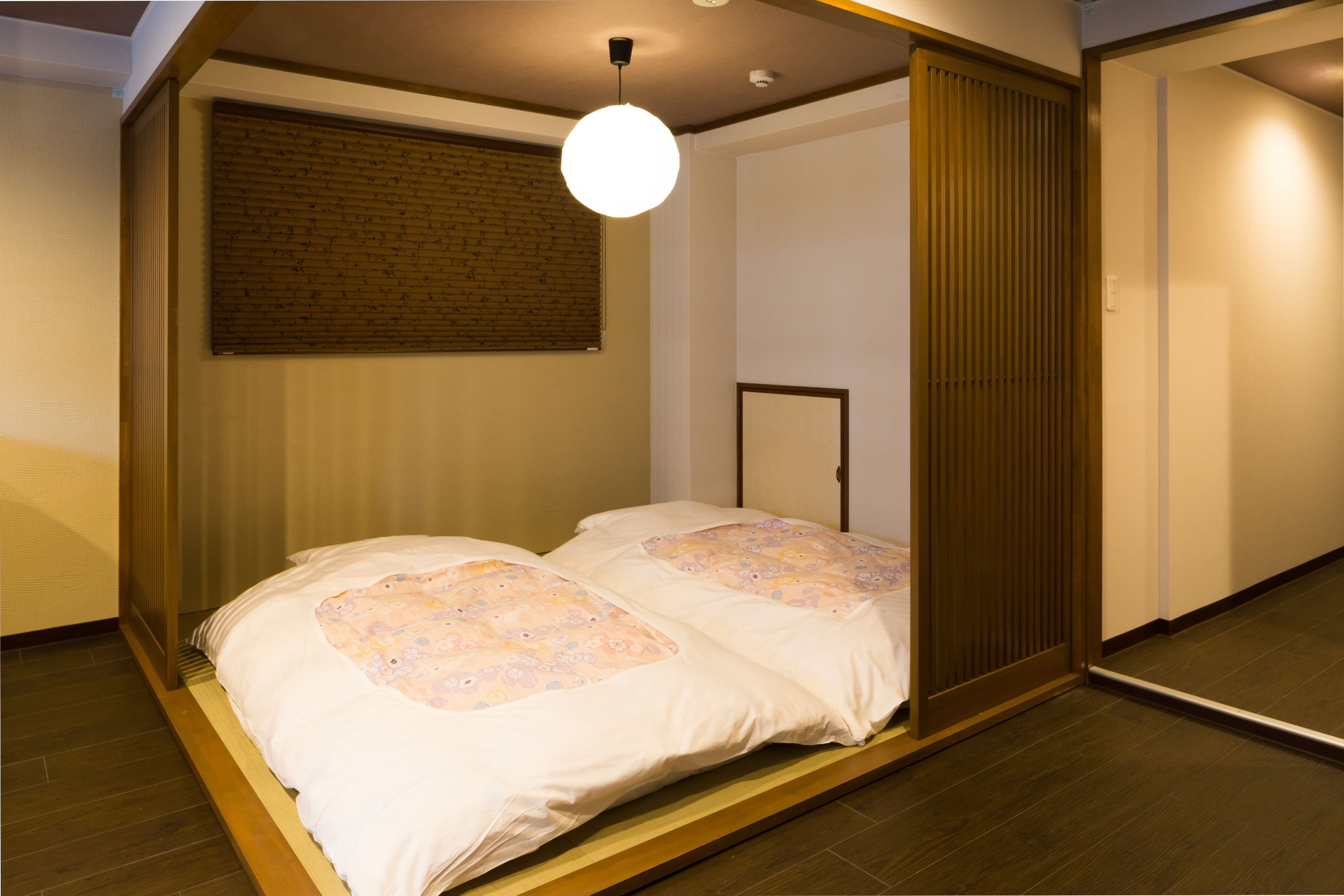 A room with a bed, a ceiling light, a window with blinds, and a wooden door.