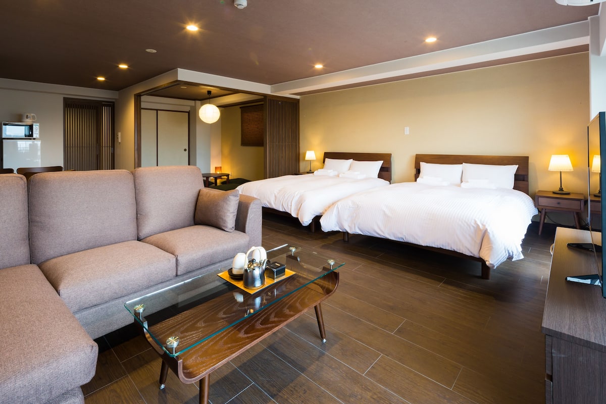 A hotel room with a sofa, a glass-top coffee table, two beds, a TV, and a microwave in the corner.