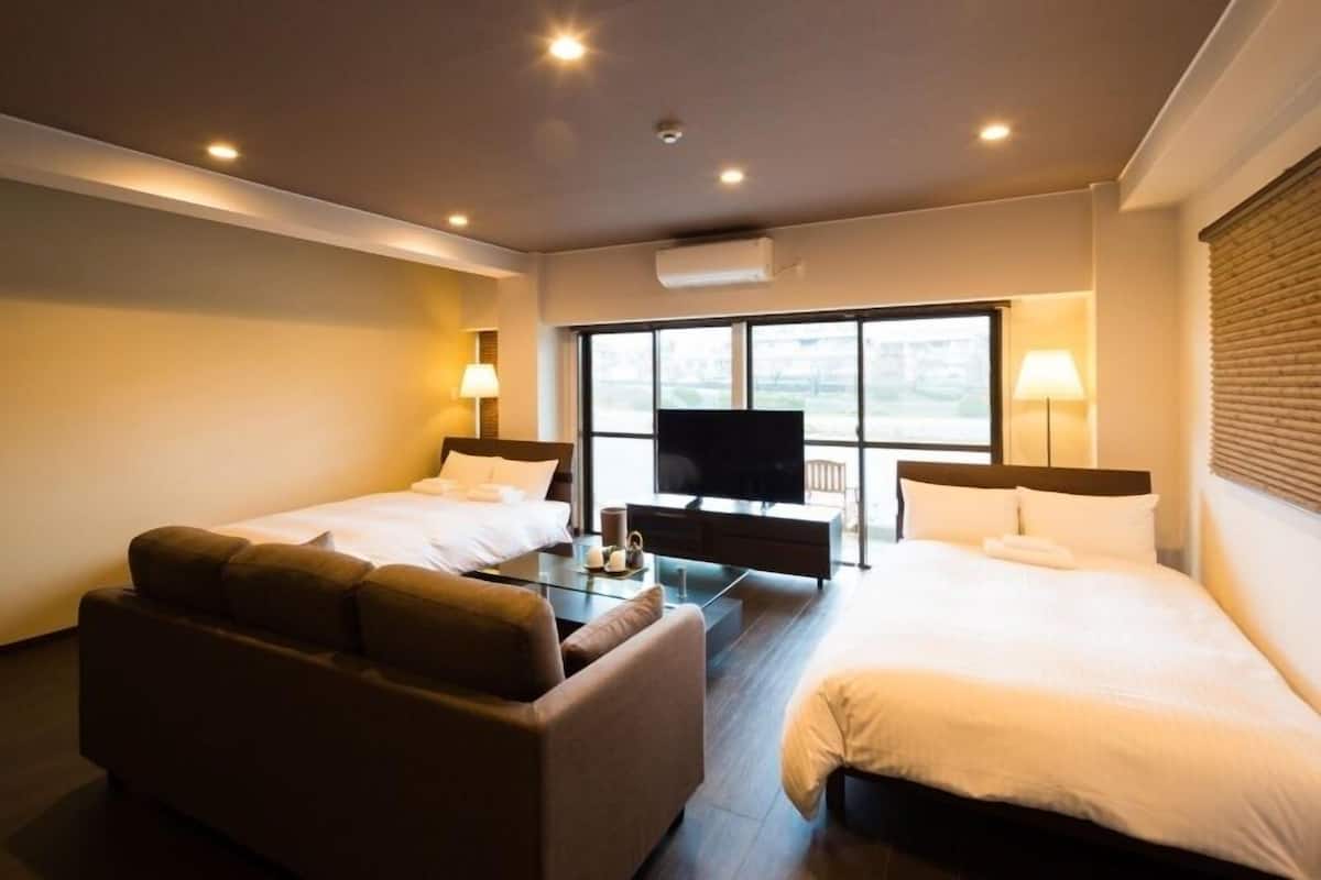 A hotel room with two beds, a sofa, a TV, and a large window.