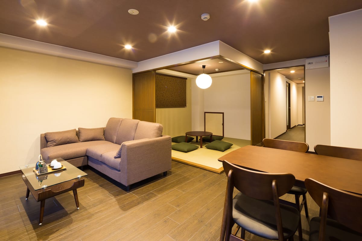 A modern living room with a sofa, a glass coffee table, a dining table with chairs, and a small side table.