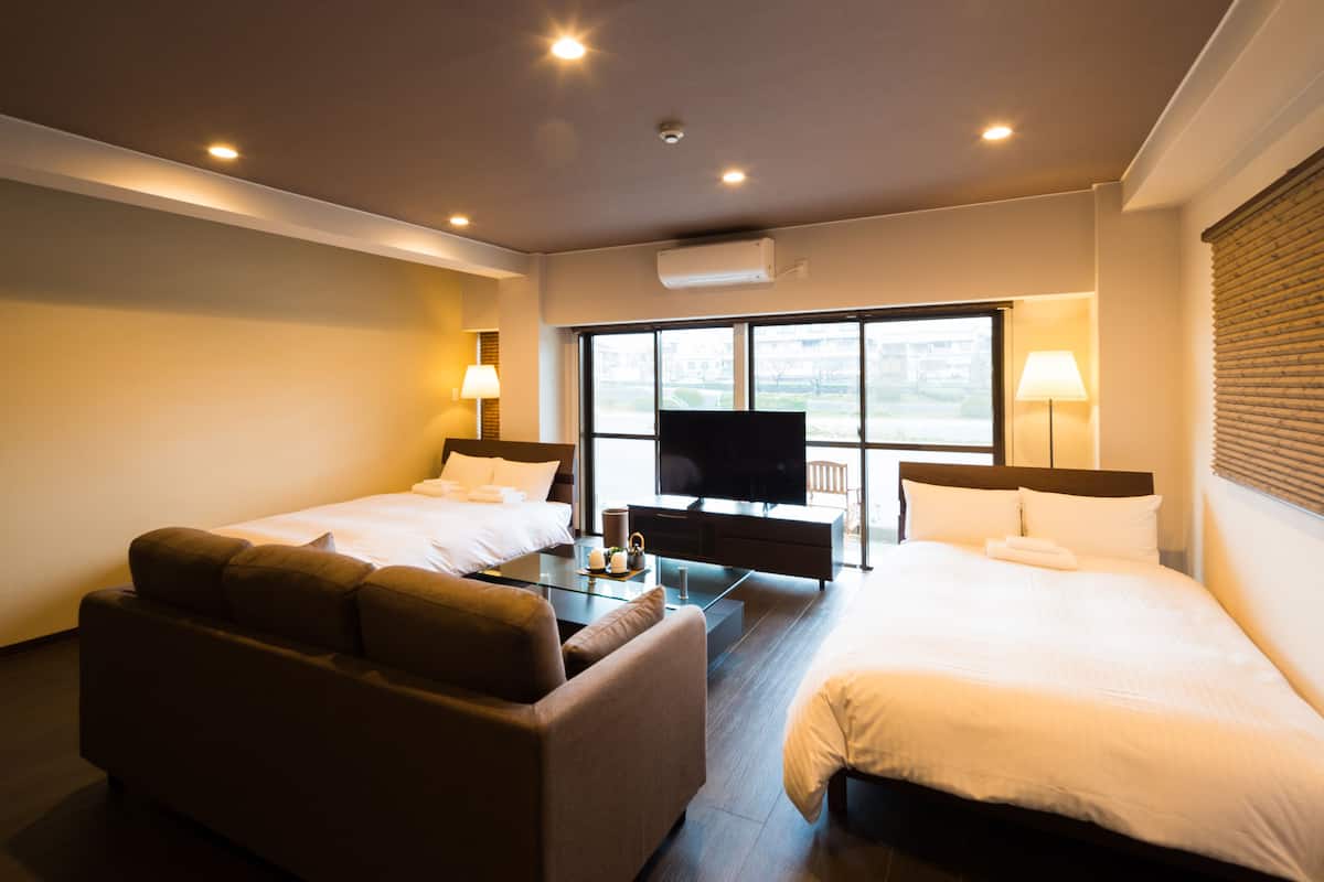 A hotel room with two beds, a sofa, a TV, and a desk.