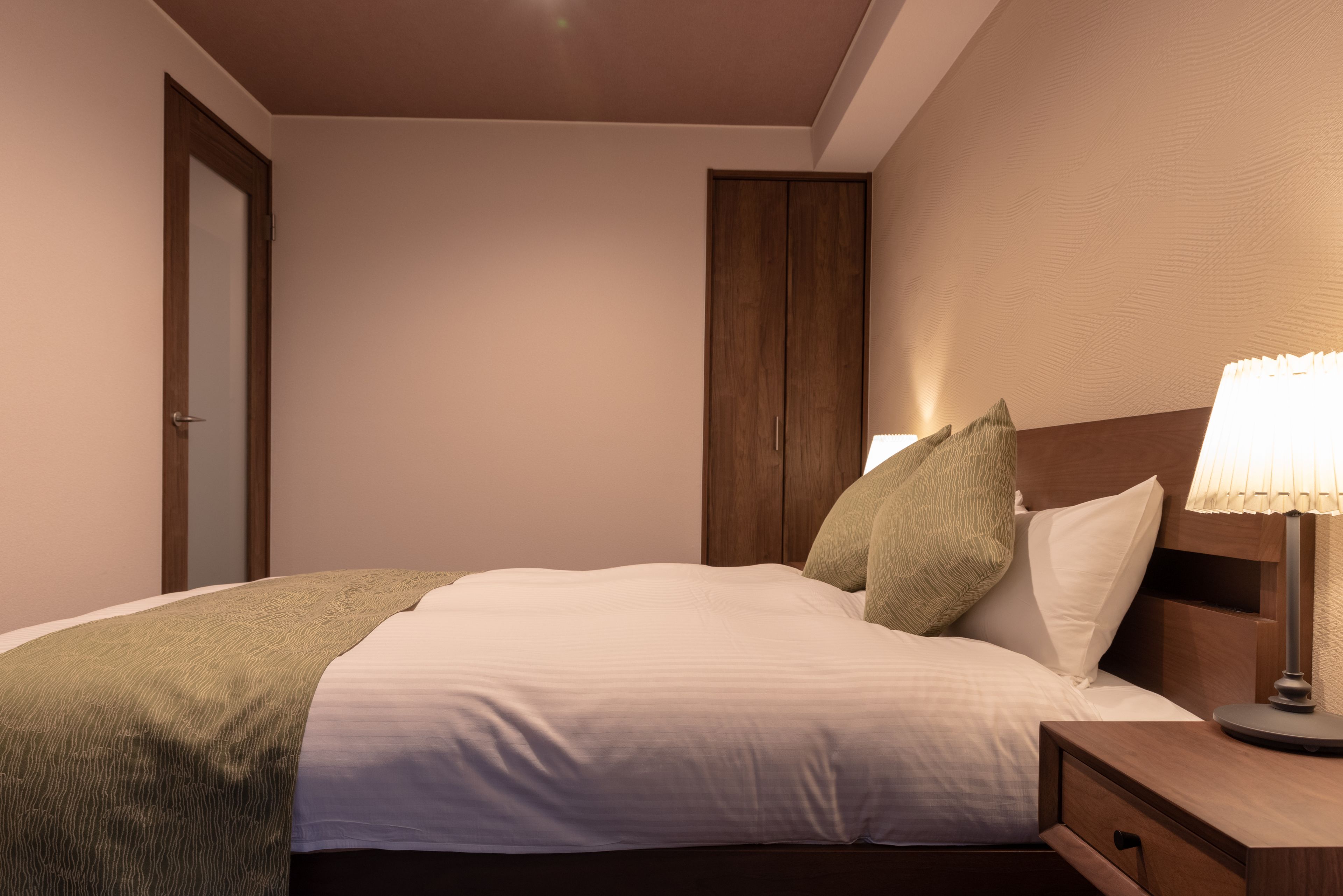 A neatly made bed with a green throw blanket, a wooden headboard, and a bedside lamp.
