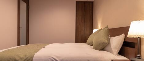 A neatly made bed with a green throw blanket, a wooden headboard, and a bedside lamp.