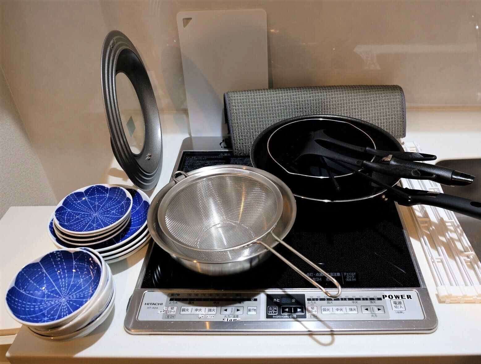 Una cocina con estufa, un colador, una sartén y una pila de tazones azules.