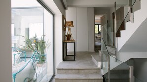 Ein modernes Interieur mit einer Treppe zu einer oberen Ebene, einer Glastrennwand und einem kleinen Tisch mit einer Lampe.