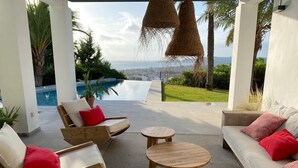 Ein überdachter Außenbereich mit Holzmöbeln und Blick auf Pool und Landschaft.