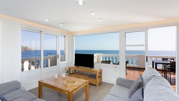 A spacious living area with a large TV, wooden coffee table, and grey sofas. It features large windows with ocean views and a balcony with a railing. - Over the Ocean with pool (Candelaria)