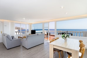 Relax in the spacious living area with a sofa, armchairs, and dining table, offering a view of the sea from the balcony.