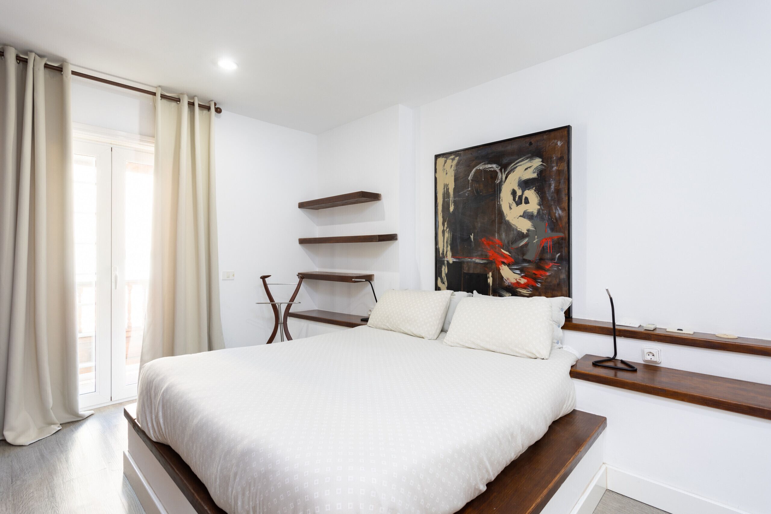 Une chambre avec un grand lit, un tableau au mur et une fenêtre avec des rideaux.