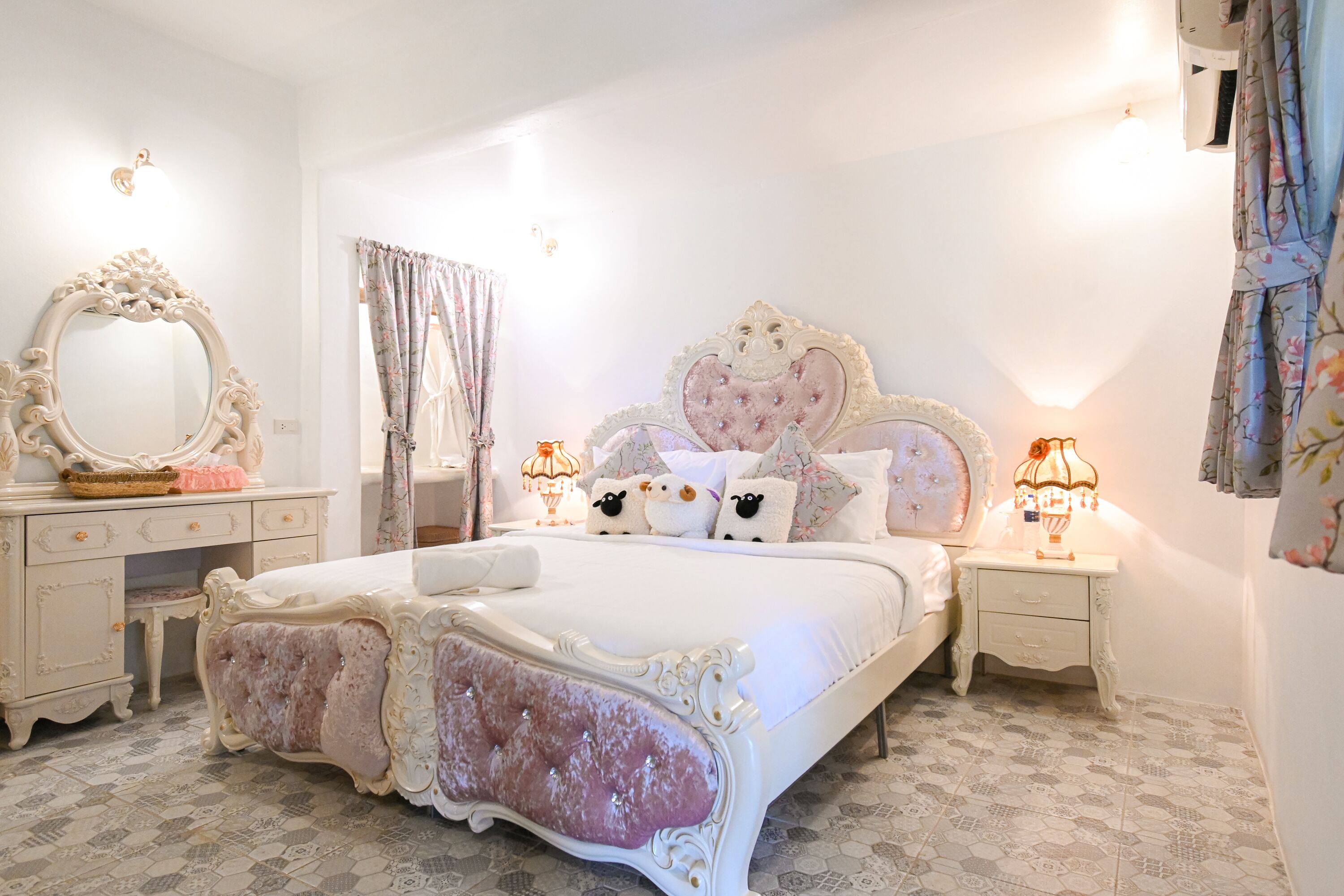 Un dormitorio con una cama grande, un cabecero decorado, un tocador con espejo y dos mesitas de noche con lámparas.