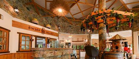 Un interior rústico con pared de piedra, vigas de madera, zona de bar y un letrero que dice 'SWISS VALLEY'.
