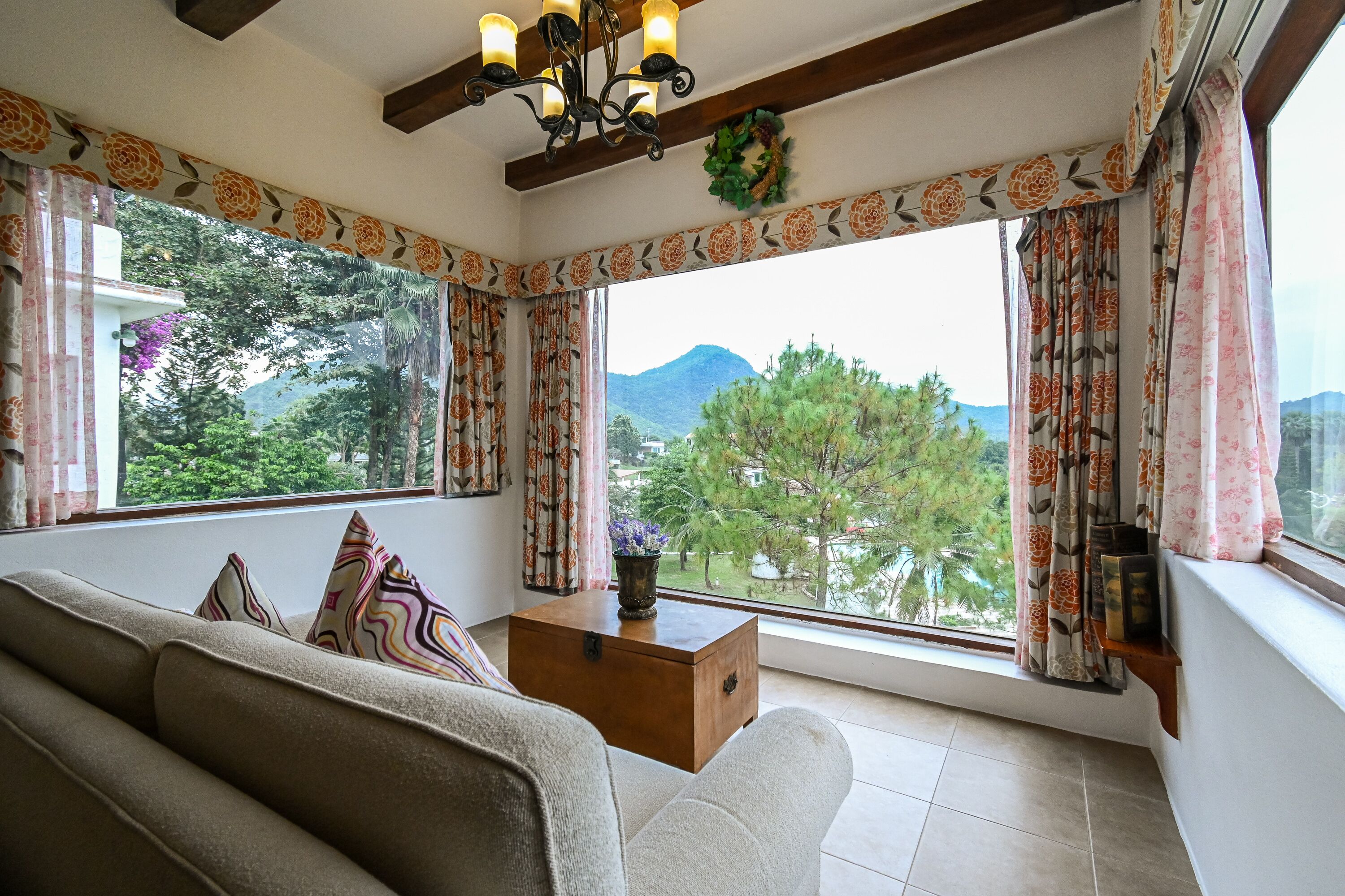 Ein Wohnzimmer mit einer Couch, einem Holztisch und Blick auf Grünflächen und Berge durch große Fenster.