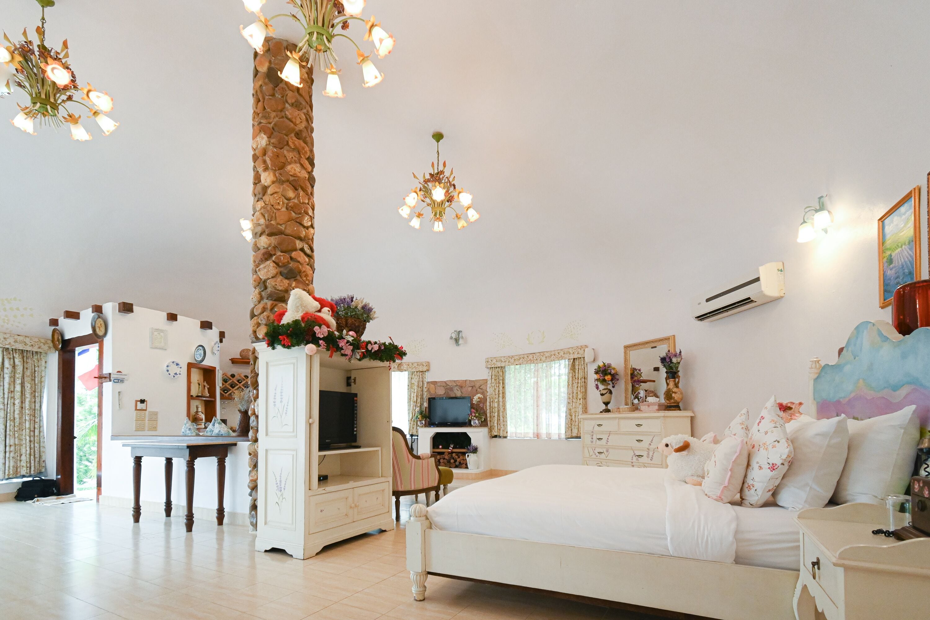A bedroom with a bed, a desk, a chair, a television, and a fireplace.