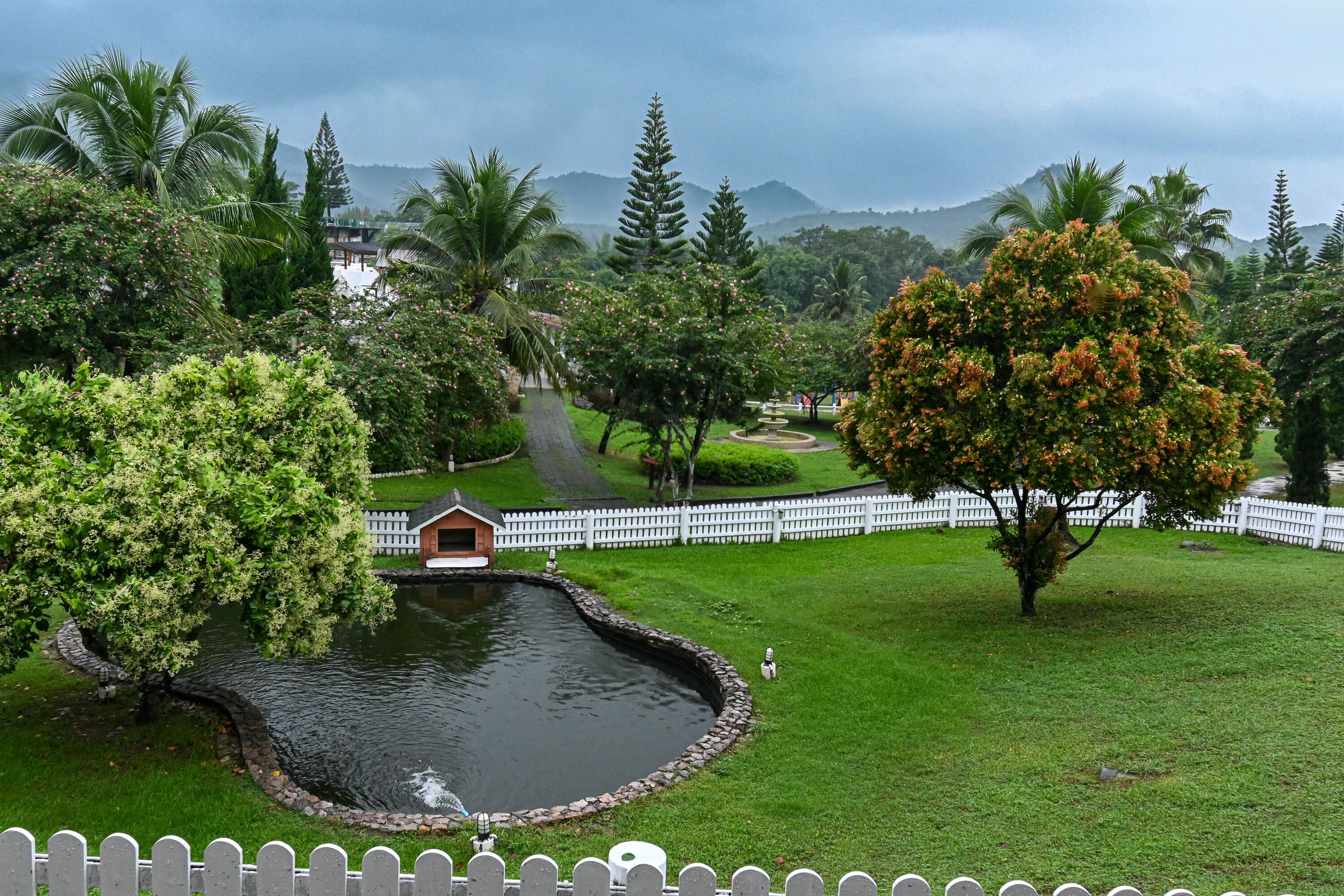Um parque com lago, cerca branca de piquete e um pequeno edifício.