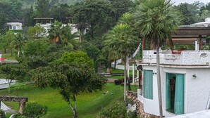 A lush green landscape with a white building featuring a stone archway and a fountain. - Swiss Valley Hip Resort (Suan Phueng)