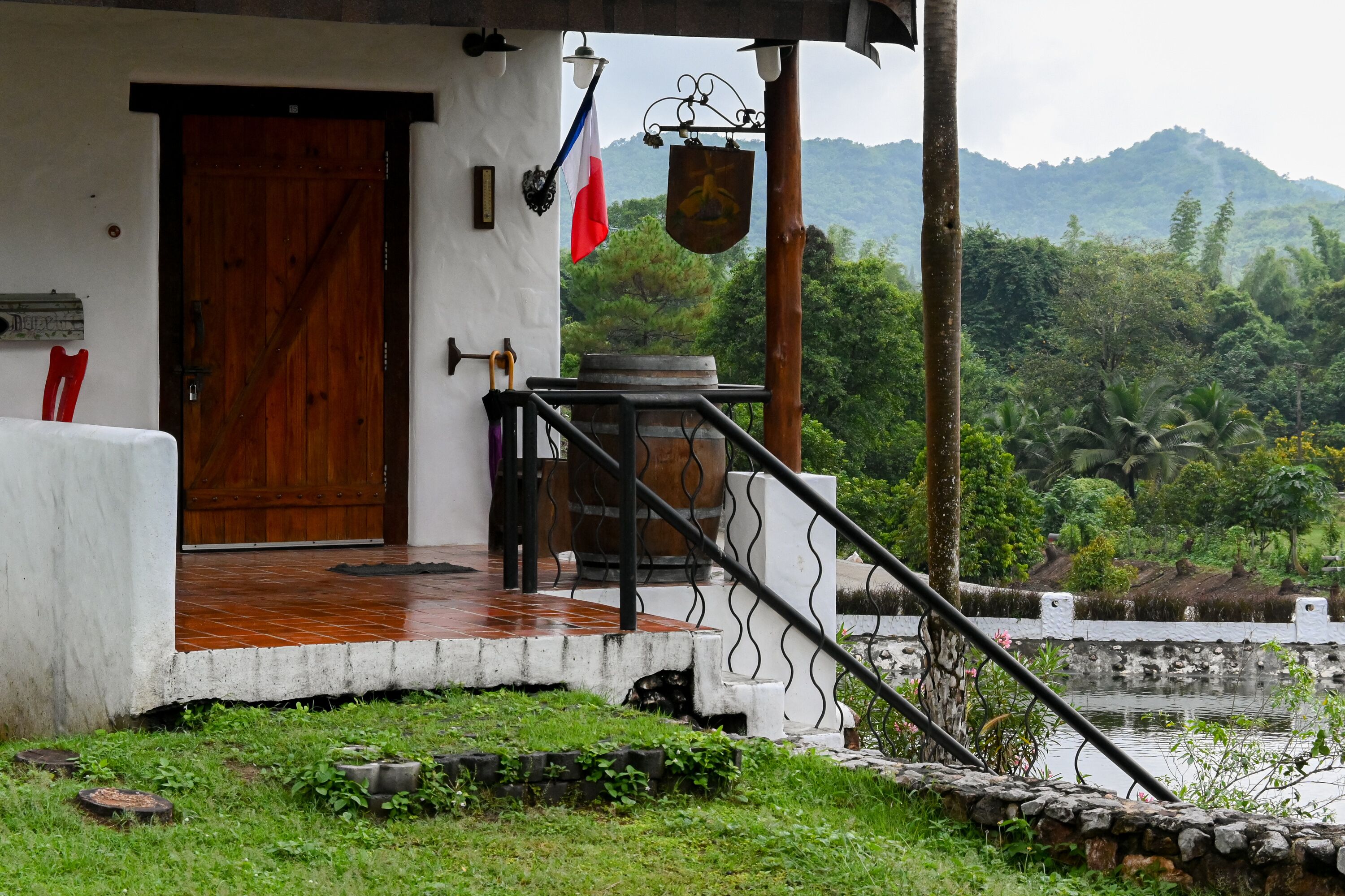 Un edificio rústico con puerta de madera, una bandera y un contenedor grande de agua en el porche.