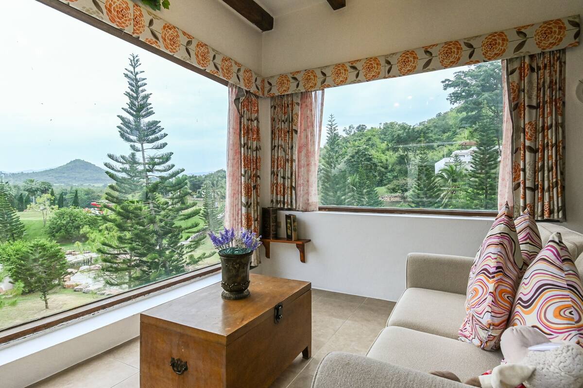 A room with a sofa, a wooden side table, and a view of a mountainous landscape through large windows.