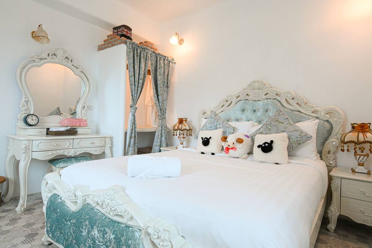 A neatly made bed with decorative pillows, a dresser with a mirror, and a lamp on the nightstand.